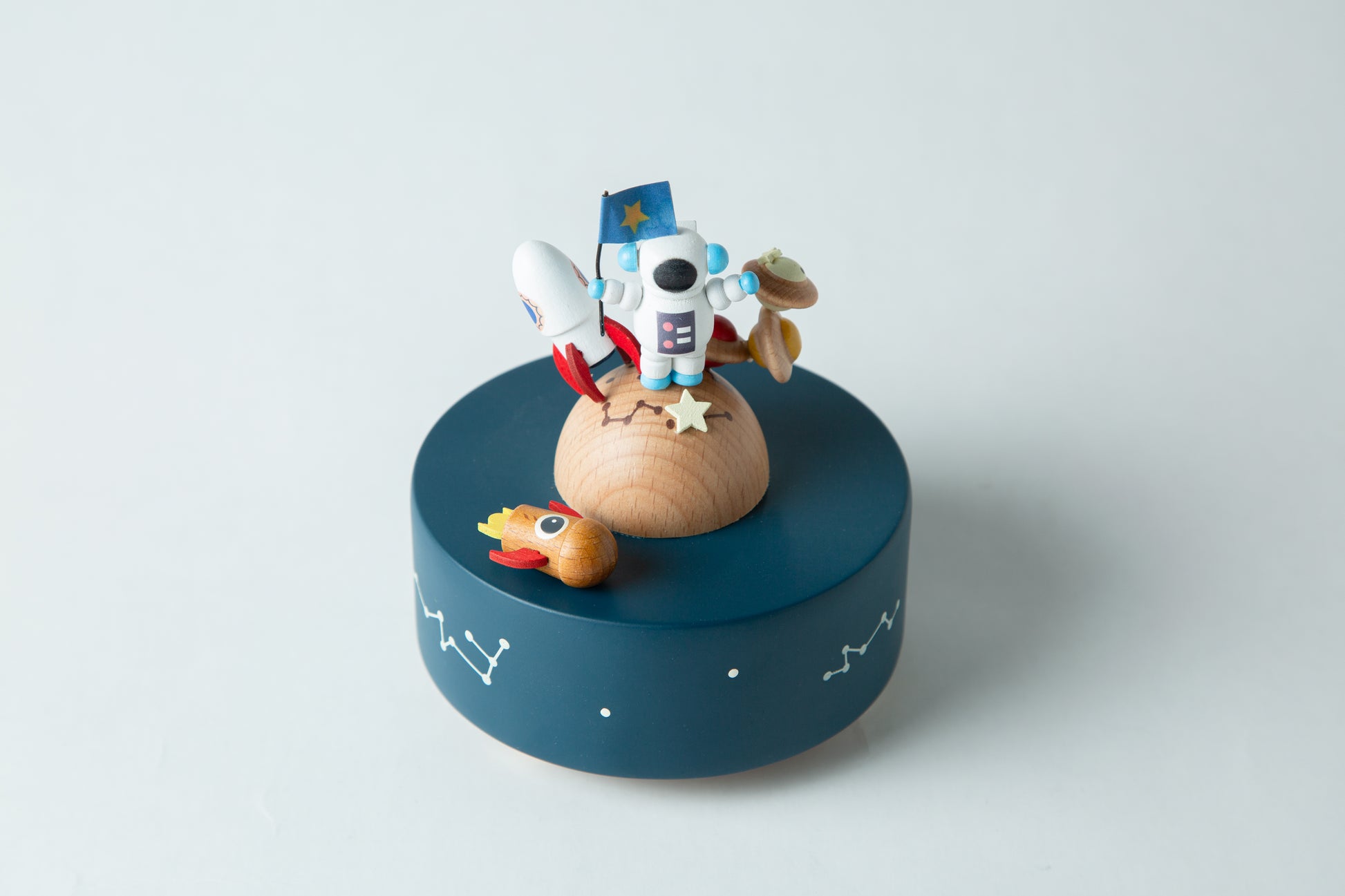 Wooden toy with astronaut design on a blue platform against a light gray background