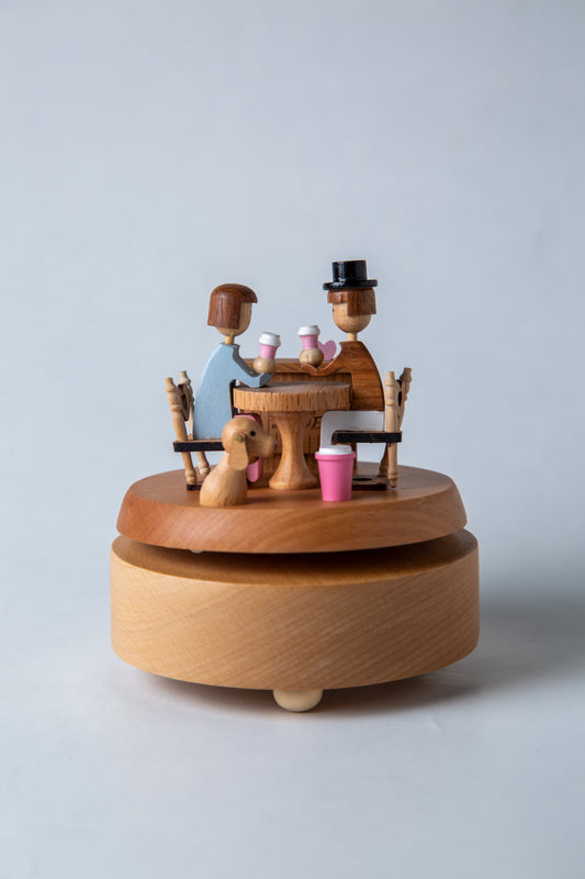 Wooden music box with a couple and dog at a table on a light gray background