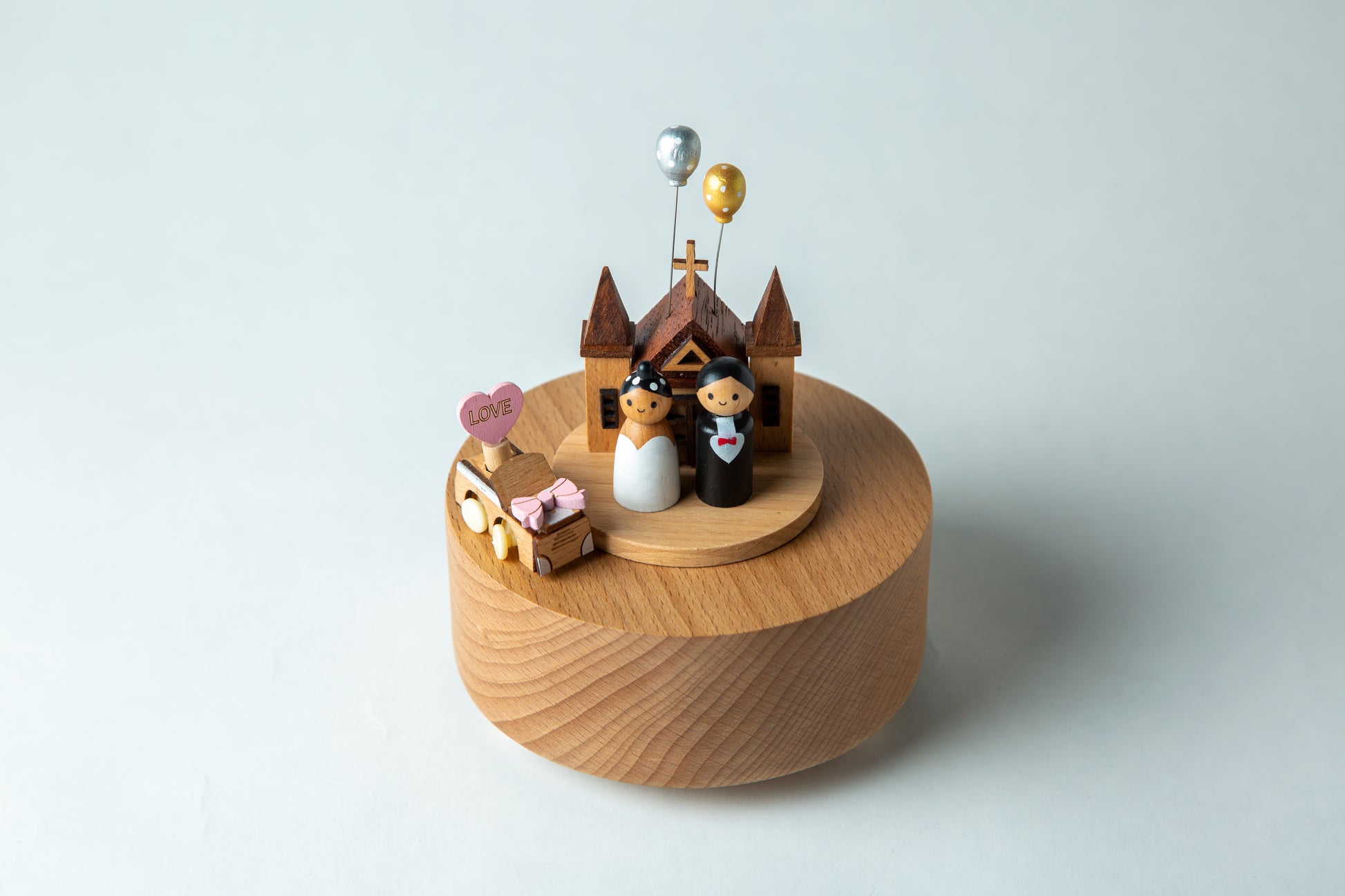 Wooden music box with wedding cake topper and figures on a light gray background