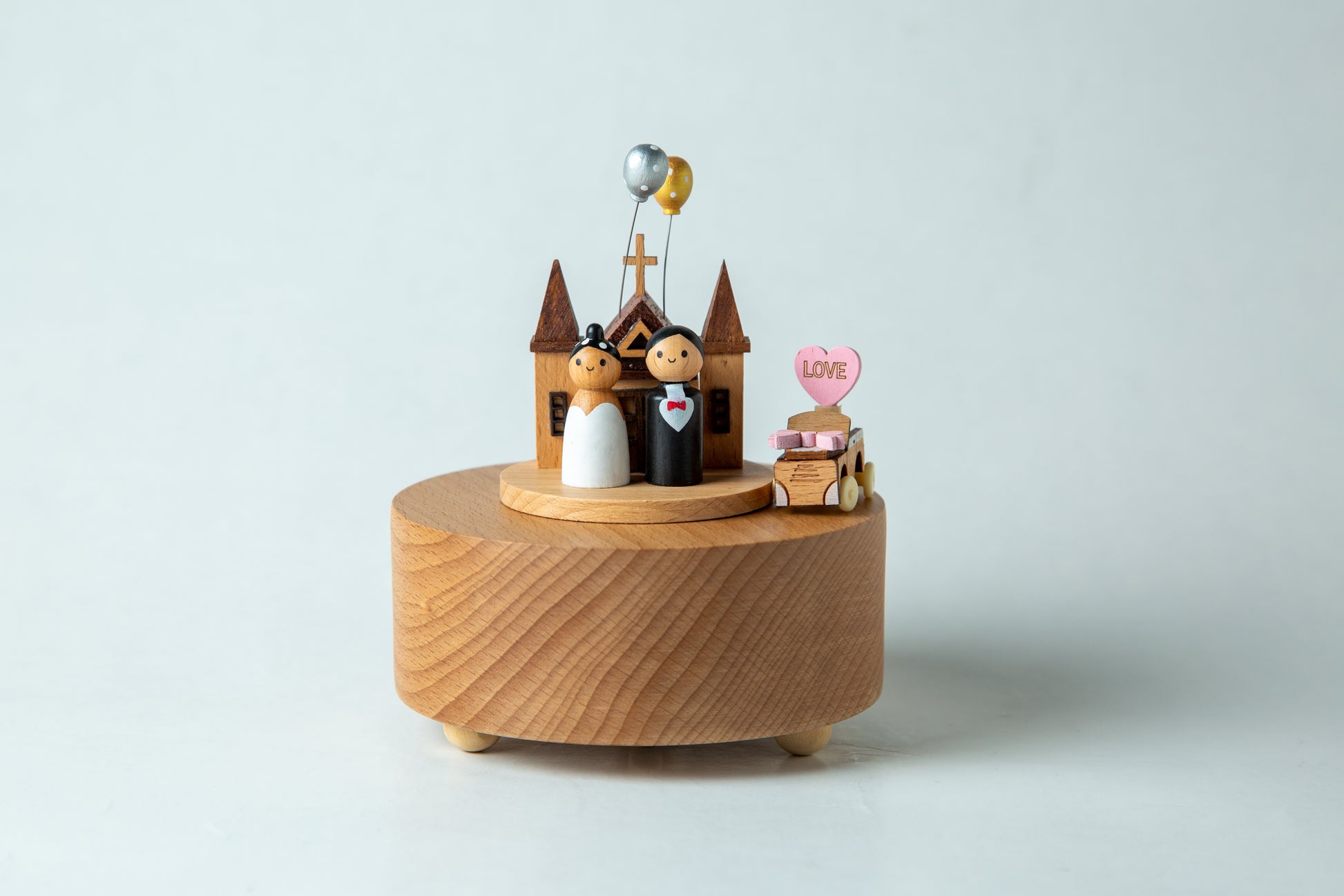 Wooden music box with wedding cake topper and couple figurines on a light gray background